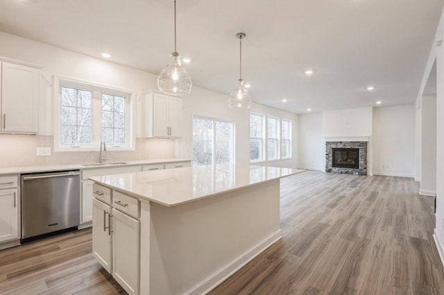 kitchen with dishwasher, white cabinets, sink, a fireplace, and a kitchen island