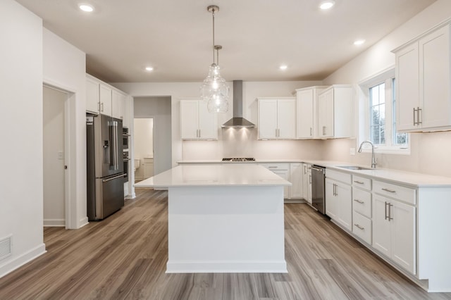 kitchen with white cabinets, appliances with stainless steel finishes, a kitchen island, and wall chimney range hood