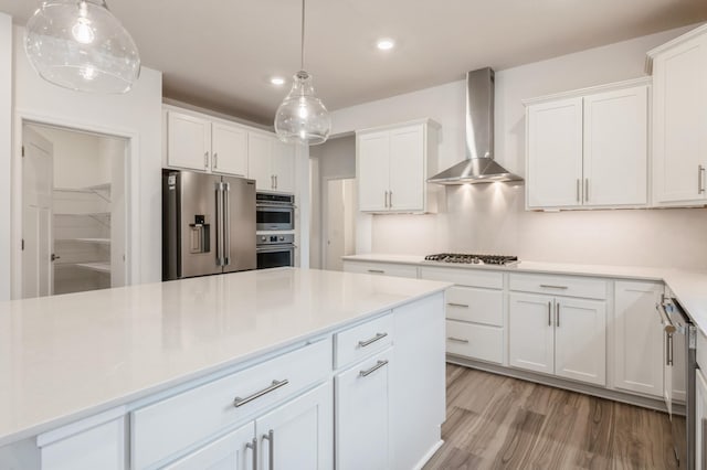 kitchen featuring white cabinets, appliances with stainless steel finishes, pendant lighting, and wall chimney exhaust hood