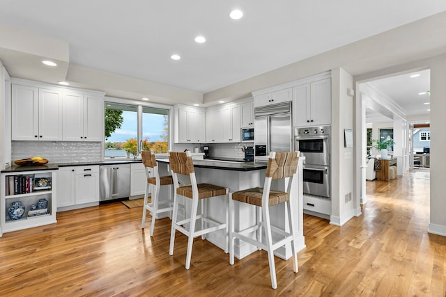 kitchen with white cabinetry, built in appliances, a kitchen breakfast bar, and light hardwood / wood-style floors