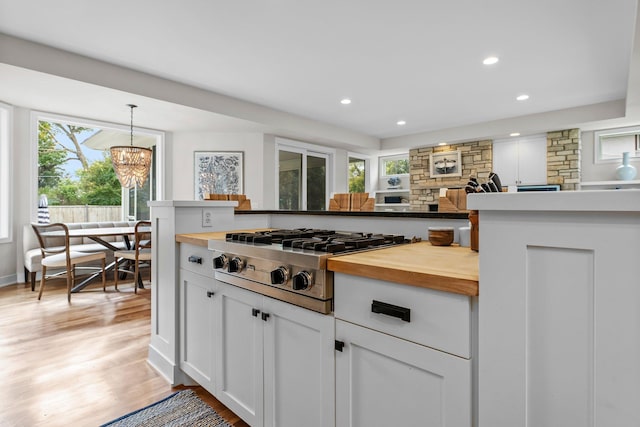 kitchen with butcher block counters, white cabinets, hanging light fixtures, stainless steel gas cooktop, and light wood-type flooring