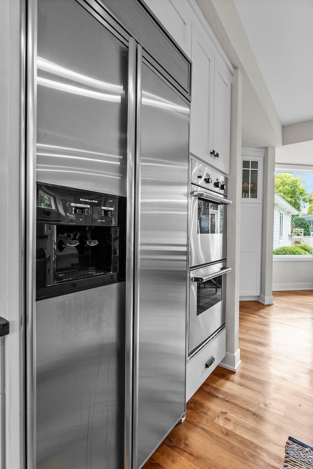 kitchen with stainless steel appliances, light hardwood / wood-style flooring, and white cabinets