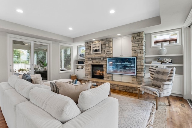 living room featuring a healthy amount of sunlight, a stone fireplace, and light hardwood / wood-style flooring