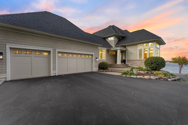 view of front of house with aphalt driveway, an attached garage, a shingled roof, a water view, and stone siding