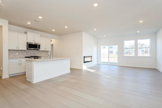 kitchen with decorative backsplash, sink, a center island with sink, white cabinets, and light hardwood / wood-style floors