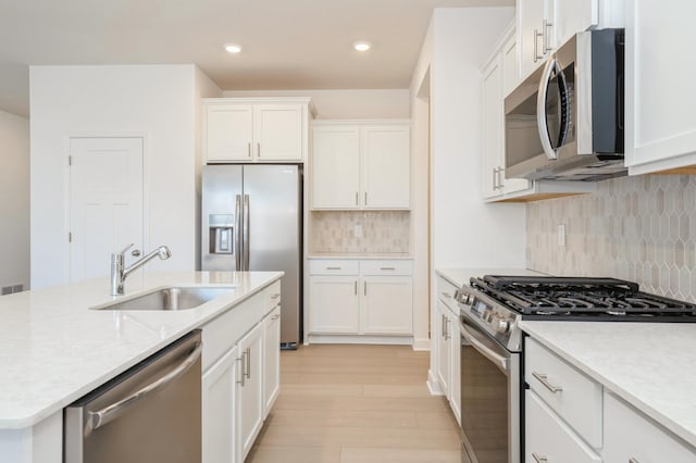 kitchen featuring backsplash, sink, light wood-type flooring, appliances with stainless steel finishes, and white cabinetry