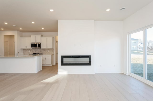 unfurnished living room featuring a healthy amount of sunlight, light wood-type flooring, and sink