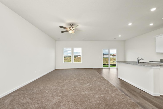 unfurnished living room with dark colored carpet, ceiling fan, and sink