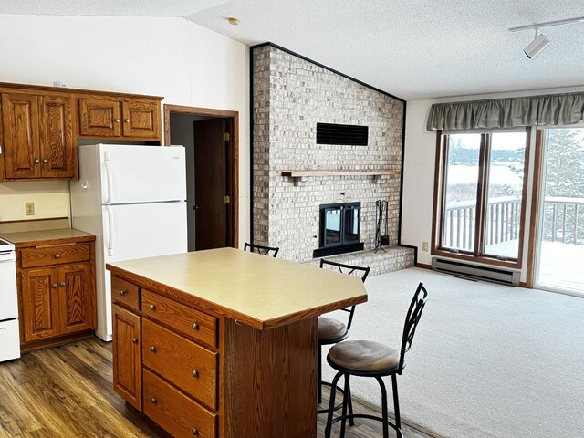 kitchen featuring vaulted ceiling, a breakfast bar, a kitchen island, baseboard heating, and white refrigerator