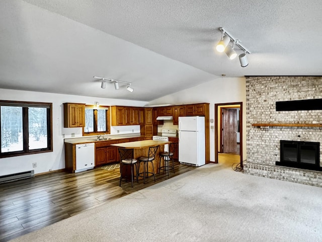 kitchen with white appliances, a textured ceiling, vaulted ceiling, a center island, and a breakfast bar area