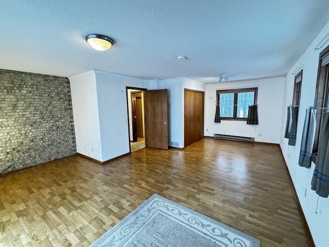 empty room with a textured ceiling, baseboard heating, brick wall, and hardwood / wood-style flooring