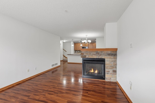 unfurnished living room featuring a textured ceiling, dark hardwood / wood-style flooring, a stone fireplace, and an inviting chandelier