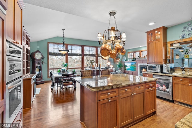 kitchen with light hardwood / wood-style flooring, decorative light fixtures, a notable chandelier, a kitchen island, and lofted ceiling