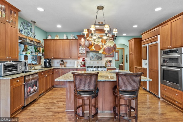 kitchen with dishwasher, light stone counters, stainless steel double oven, a kitchen island, and sink