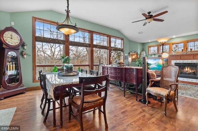 dining area featuring ceiling fan with notable chandelier, a tile fireplace, vaulted ceiling, and wood-type flooring