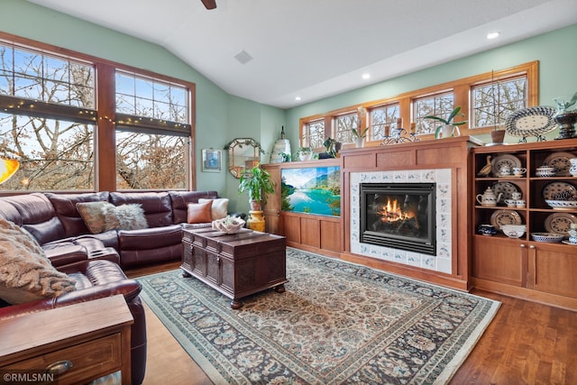 living room with a healthy amount of sunlight, a tile fireplace, vaulted ceiling, and wood-type flooring