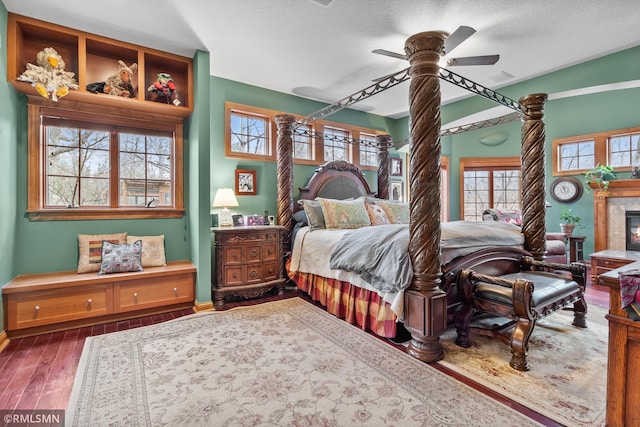 bedroom with a tiled fireplace, a textured ceiling, ceiling fan, and dark hardwood / wood-style floors