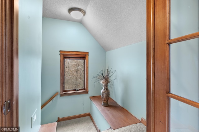 interior space featuring a textured ceiling, vaulted ceiling, and carpet flooring