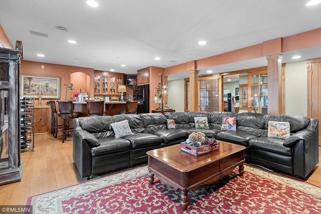 living room with decorative columns, light wood-type flooring, and bar