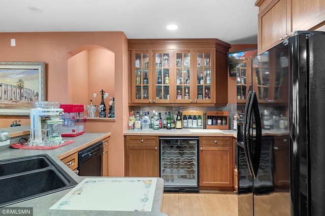 kitchen featuring black appliances, beverage cooler, light wood-type flooring, backsplash, and sink