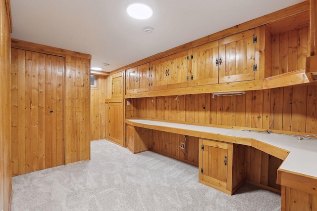 unfurnished office with built in desk, light colored carpet, and wood walls