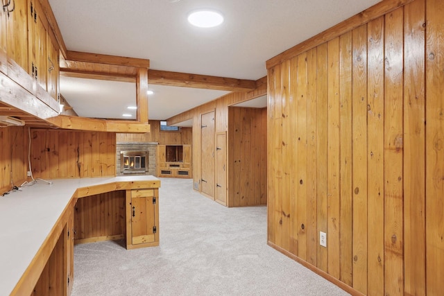 kitchen featuring wood walls, a fireplace, beamed ceiling, and light colored carpet