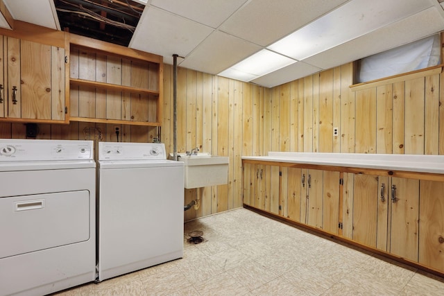 laundry area featuring wood walls, sink, cabinets, and independent washer and dryer