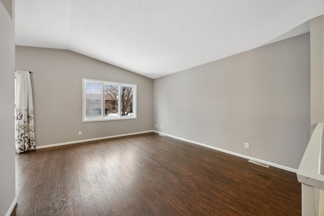 empty room with vaulted ceiling, a textured ceiling, and dark hardwood / wood-style flooring