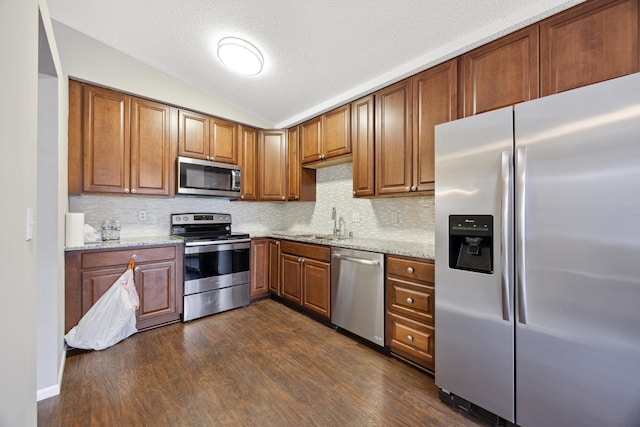 kitchen with lofted ceiling, sink, dark hardwood / wood-style flooring, stainless steel appliances, and light stone countertops