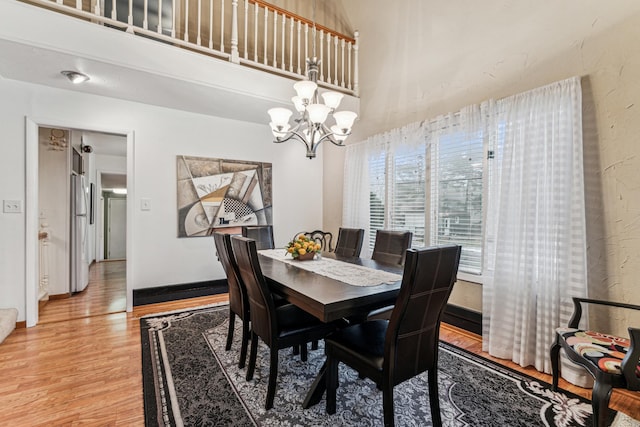 dining space featuring a notable chandelier, wood-type flooring, and a high ceiling