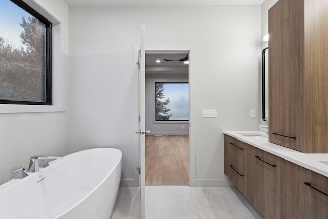 full bathroom with a soaking tub, a healthy amount of sunlight, baseboards, and double vanity