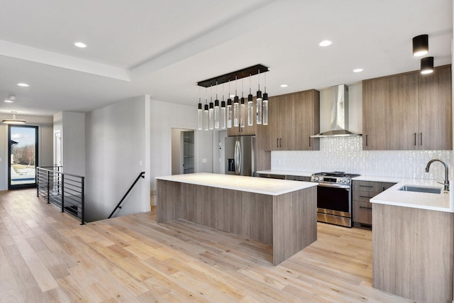 kitchen with sink, appliances with stainless steel finishes, hanging light fixtures, a center island, and wall chimney exhaust hood