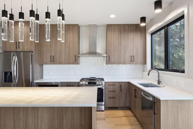 kitchen featuring sink, hanging light fixtures, wall chimney exhaust hood, stainless steel appliances, and light hardwood / wood-style flooring