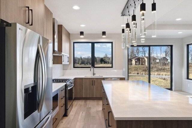 kitchen with sink, light hardwood / wood-style flooring, appliances with stainless steel finishes, pendant lighting, and wall chimney range hood