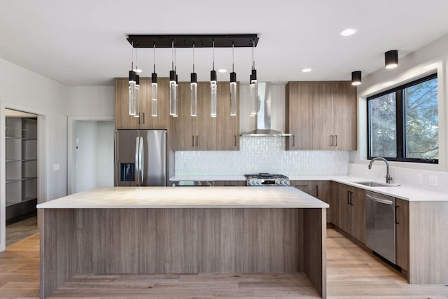 kitchen with hanging light fixtures, stainless steel appliances, wall chimney exhaust hood, and a kitchen island