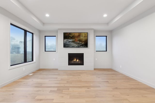 unfurnished living room featuring a wealth of natural light, a fireplace, light wood-type flooring, and a tray ceiling