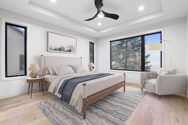 bedroom with light hardwood / wood-style floors, a raised ceiling, and ceiling fan