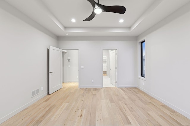 unfurnished bedroom featuring connected bathroom, a tray ceiling, and light hardwood / wood-style floors