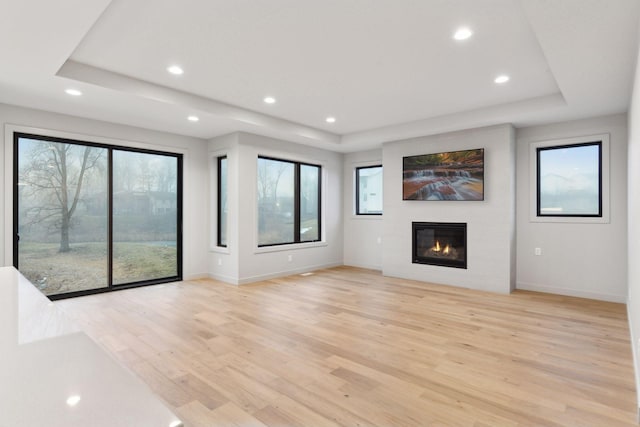 unfurnished living room featuring a tray ceiling, light wood-type flooring, and a wealth of natural light