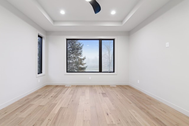 unfurnished room featuring recessed lighting, a tray ceiling, baseboards, and light wood-style flooring