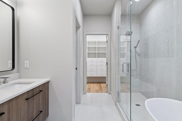 full bathroom featuring a shower stall, a freestanding bath, vanity, and a walk in closet