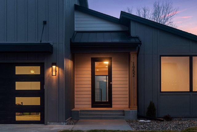 exterior entry at dusk with a standing seam roof, a garage, and metal roof