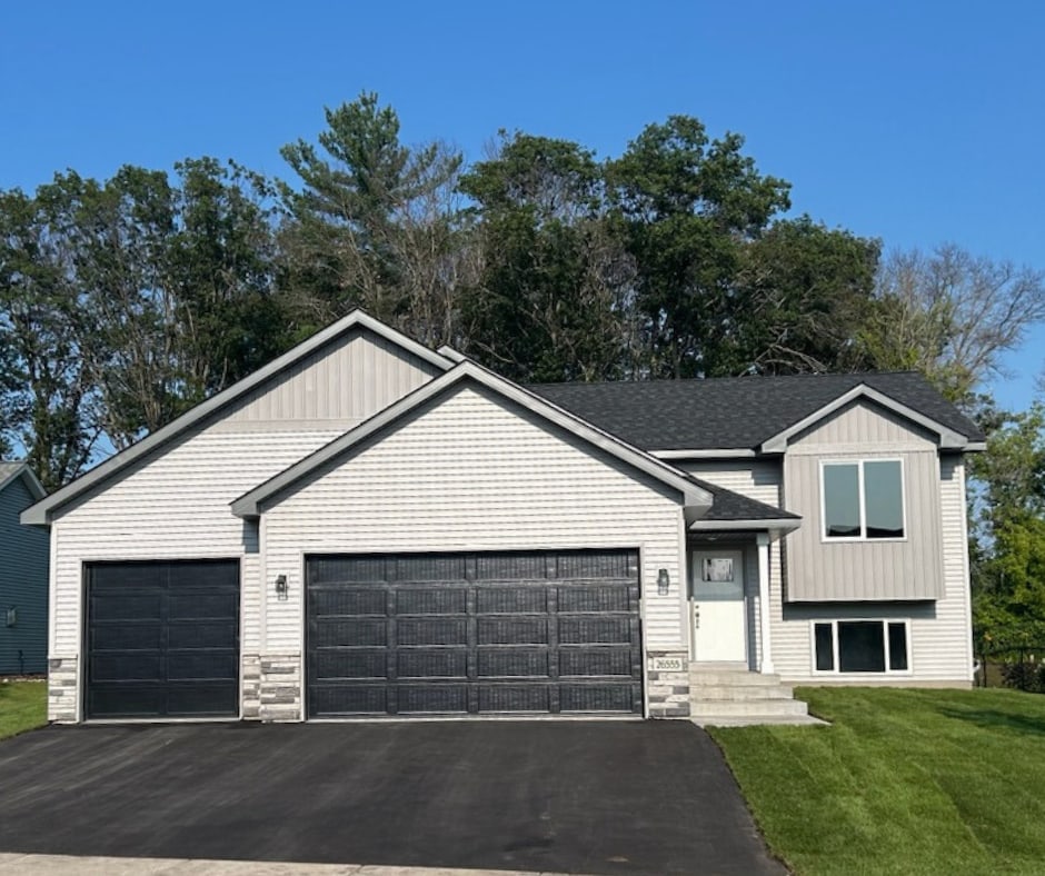 tri-level home with a garage, stone siding, a front yard, and driveway