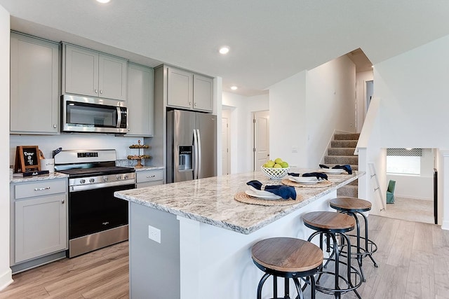 kitchen with light stone countertops, a kitchen bar, gray cabinetry, stainless steel appliances, and light hardwood / wood-style floors