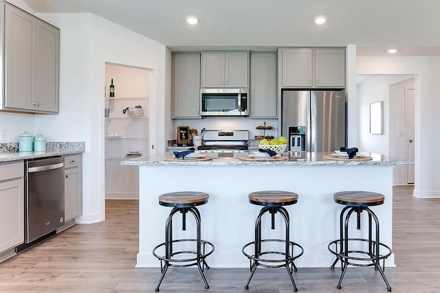 kitchen with light hardwood / wood-style flooring, gray cabinets, appliances with stainless steel finishes, a kitchen island, and light stone counters