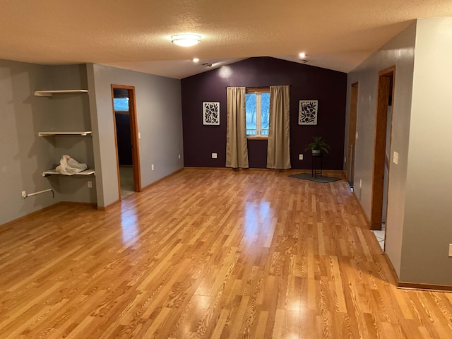 interior space featuring a textured ceiling, light hardwood / wood-style floors, and lofted ceiling