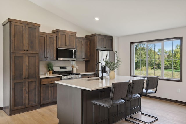 kitchen featuring dark brown cabinetry, sink, stainless steel appliances, an island with sink, and light hardwood / wood-style floors