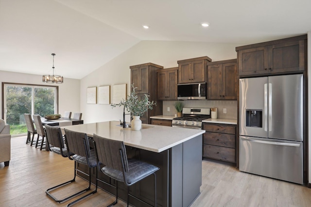 kitchen with pendant lighting, stainless steel appliances, a center island with sink, and light hardwood / wood-style floors