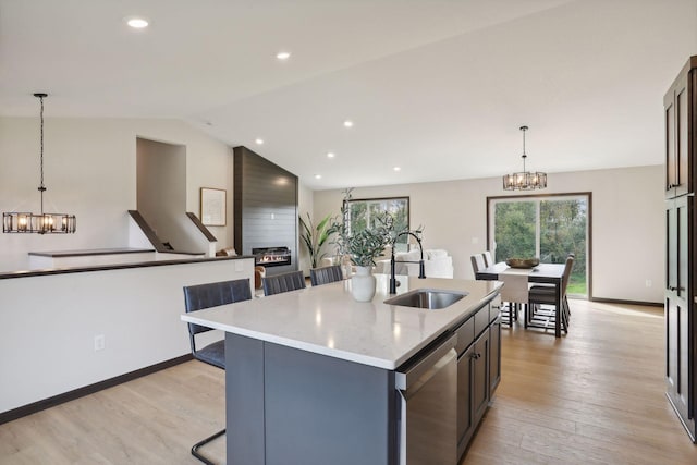 kitchen with stainless steel dishwasher, a large fireplace, sink, pendant lighting, and a center island with sink