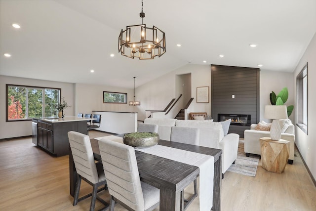 dining area with a notable chandelier, a fireplace, lofted ceiling, and light wood-type flooring